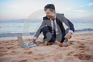 young man in suit with laptop working on the beach and talking to someone