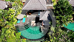 Young man sunbathing by the pool in luxury bungalow in tropical garden. Asian man tanning enjoying summer day