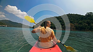 Man with sunglasses and hat rows pink plastic canoe along sea ag