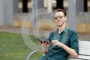 A young man in sunglasses is holding a tablet in his hands