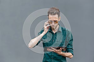 A young man in sunglasses is holding a tablet in his hands and talking on the phone