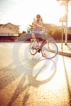 Young man in sunglasses riding a bicycle on a city street at sun