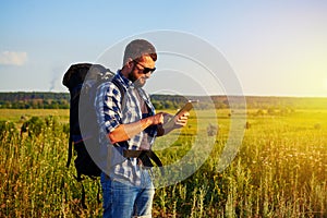 Young man in sunglasses with rucksack and data tablet against sunset field background