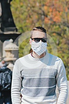 Young man with sunglasses and sewed fabric face mask photographed on the Charles Bridge in Prague, Czech Republic. Blurred