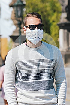 Young man with sunglasses and sewed fabric face mask photographed on the Charles Bridge in Prague, Czech Republic. Blurred