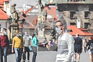 Young man with sunglasses and sewed fabric face mask photographed on the Charles Bridge in Prague, Czech Republic. Blurred people