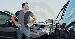 Young man in sunglasses sits stressed out after a car crash on the road. The concept of traffic accidents and insurance.