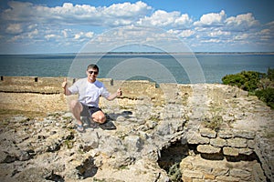 Young man in sunglasses sits on the wall of the fortress by the sea