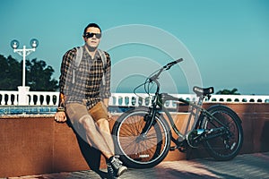 Young Man In Sunglasses Sitting On Fountain Next To Bicycle In Summer Park Daily Lifestyle Urban Resting Concept