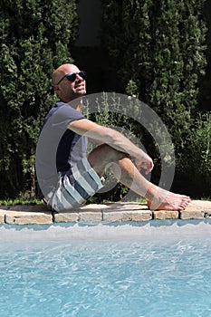 Young man in sunglasses and t-shirt sitting poolside while looking away