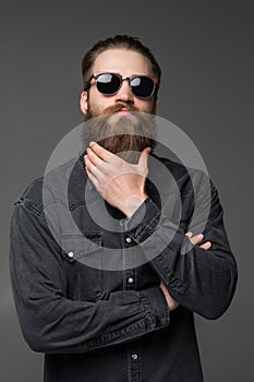 Young handsome man in sunglasses touch his long beard isolated on gray background photo