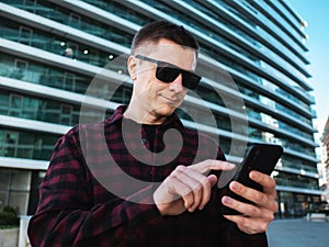 Young man in sunglasses using mobile phone in hands at modern new office building background