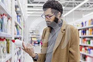 Young man in the supermarket in the household chemicals department. Large selection of products. A brunette with glasses and a bea