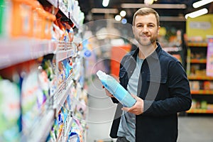 Young man in the supermarket in the household chemicals department. Large selection of products. A brunette in a glasses