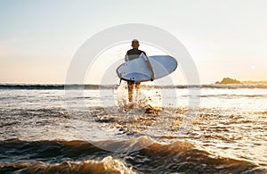 Young man Surfer taking surfboard and comming with long surf board to waves on the evening sunset sky background. Active holidays photo