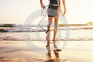 Young man Surfer taking surfboard and comming with long surf board to waves on the evening sunset sky background. Close up legs photo