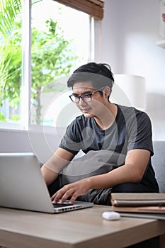 Young man surfing internet with computer laptop in living room.