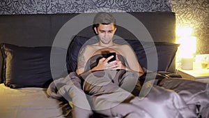 Young man surfing internet while lying in bed in the bedroom at night