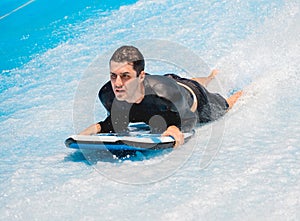 Young man surfing on a wave simulator at a water amusement park