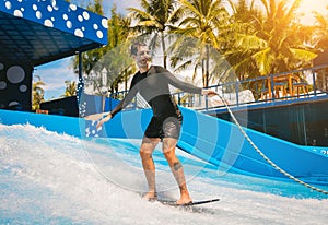 Young man surfing on a wave simulator at a water amusement park