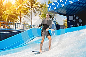 Young man surfing on a wave simulator at a water amusement park