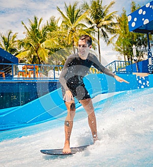 Young man surfing on a wave simulator at a water amusement park