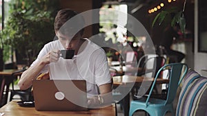 Young man surfing website and chatting, freelancer and blogger working as a graphic designer indoor, and drinking coffee