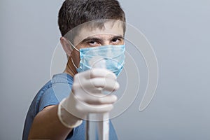 Young man in surgical mask holding up bottle of disinfectant spray on a gray studio background, fight against spread of infection