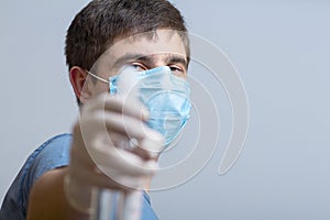 Young man in surgical mask holding up bottle of disinfectant spray on a gray studio background, fight against spread of infection
