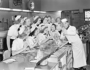 Young man surrounded by a group of college women in his soda fountain