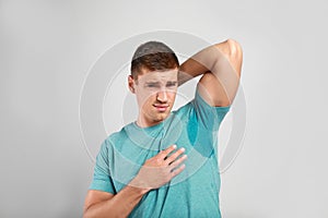 Young man with sweat stain on his clothes against light background