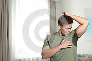 Young man with sweat stain on his clothes, space for text. Using deodorant