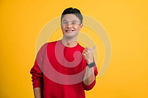 Young man in sweater showing thumb up looking camera isolated on yellow colour background, studio portrait. Happy New Year