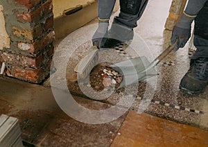 A young man sweeps construction debris into a dustpan indoors.