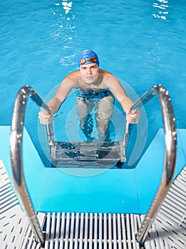 Young man swimmer with hat and goggles getting out of pool