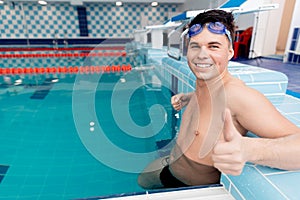 Young man swimmer showing good thumb sign in pool, swimming competition concept