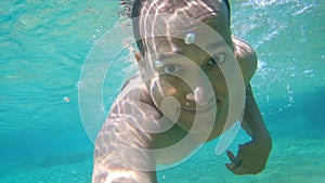 Young man swimming in blue clear under water of waterfall with many rocks from flat angle