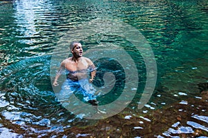 Young man swimming in natural waterfall clear water at morning from top angle