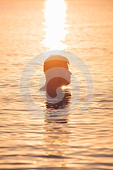 young man swimming in sea at sunset