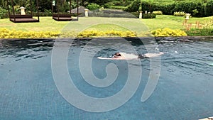A young man swims in the style of a Front crawl in an outdoor pool in a tropical garden