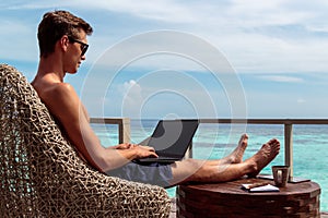 Young man in swimsuit working on a laptop in a tropical destination