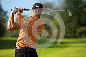 Young man swinging golf club, rear view