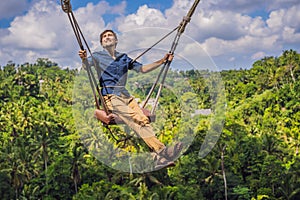 Young man swinging in the jungle rainforest of Bali island, Indonesia. Swing in the tropics. Swings - trend of Bali