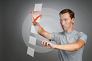 Young man in t-shirt checking on checklist box. Gray background.