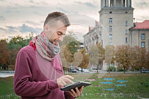 Young man with tablet in hands outdoors in urban public space