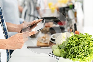Young man with tablet PC reading recipes in kitchen