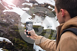 A young man takes a picture of a waterfall on a mobile phone in