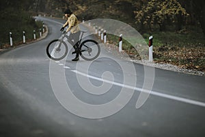 Young man taking a brake on a country road during biking through autumn forest