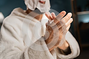 A young man taking care of the skin of his hands in the evening in the bedroom applies moisturizing cream to his hands