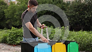 Young man taking from eco packager garbage and put them into recycling bins outddors. Concept of recycling. Tree bins